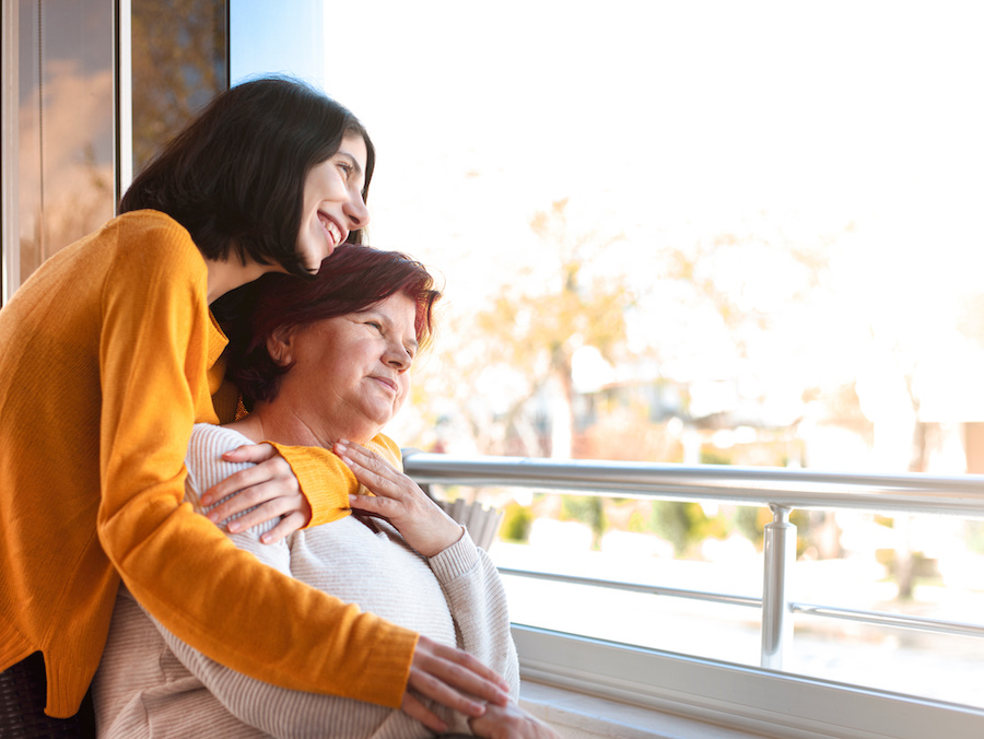 Happy senior mother and adult daughter looking at the view through the window.